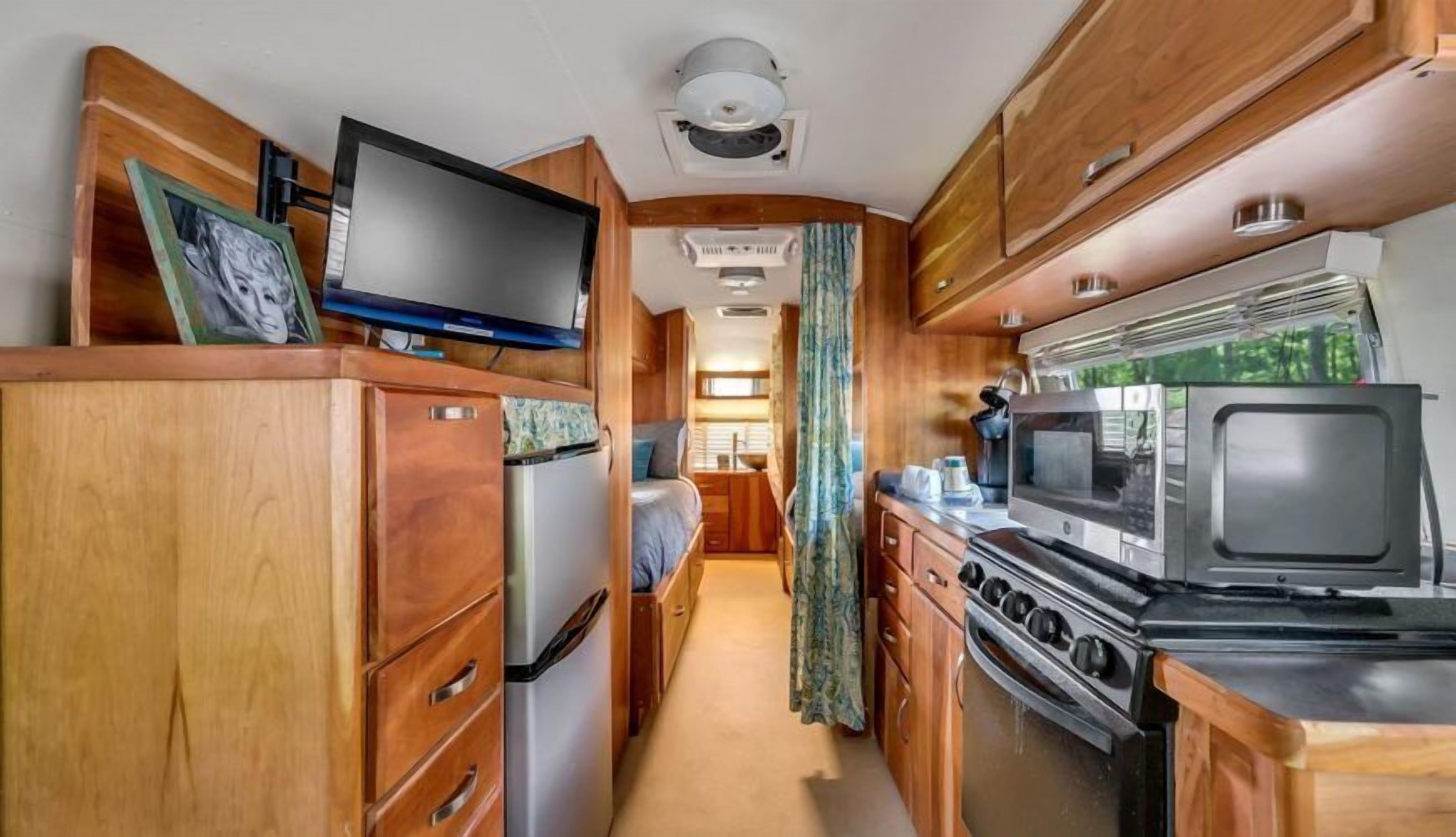 Une cuisine compacte pour camping-car, dotée de meubles en bois, d’un réfrigérateur, d’un four à micro-ondes et d’une cuisinière.