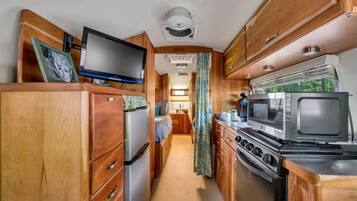 Une cuisine compacte pour camping-car, dotée de meubles en bois, d’un réfrigérateur, d’un four à micro-ondes et d’une cuisinière.