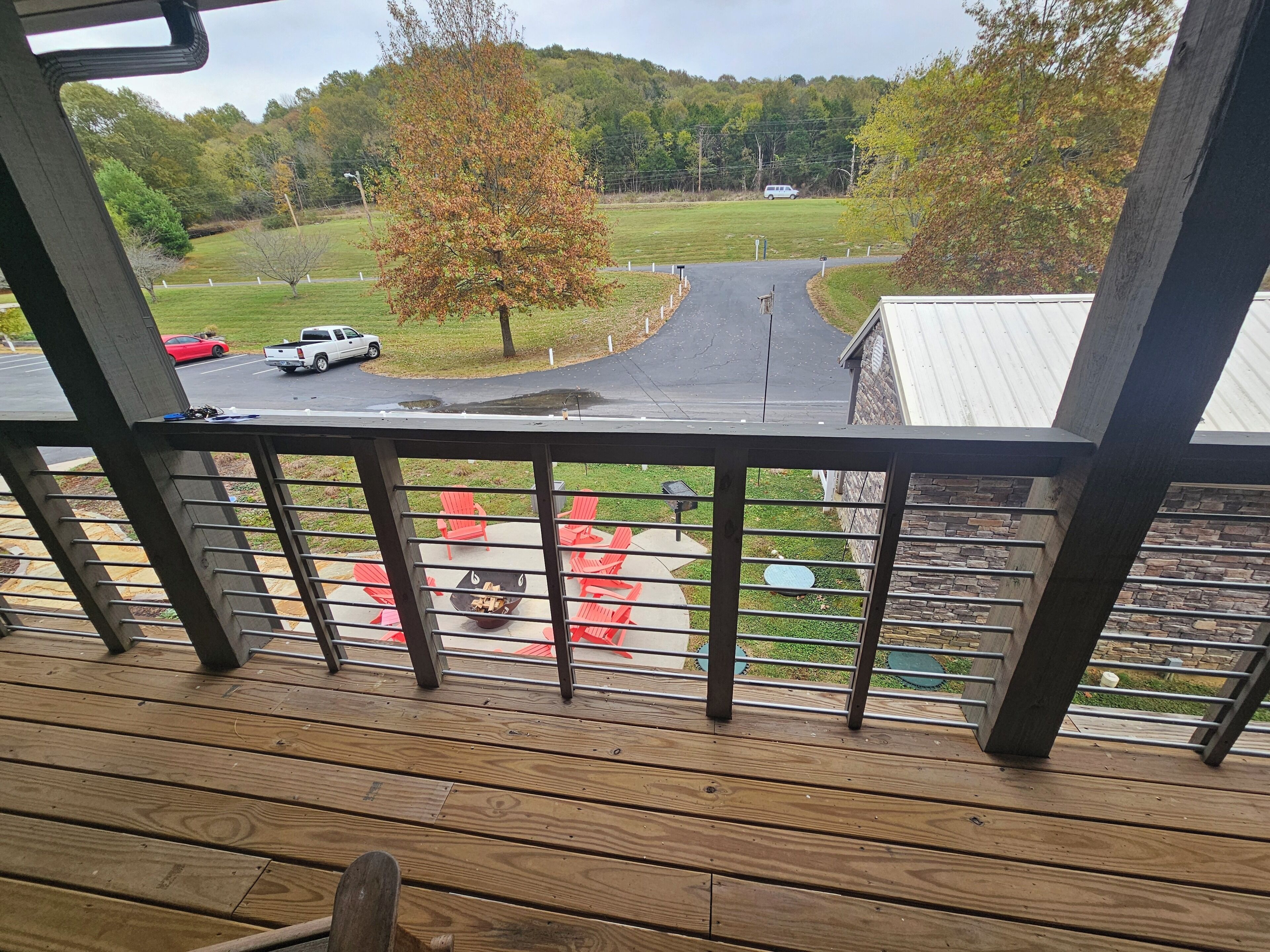 A wooden deck with a view of a road, a tree, and a building in the background.
