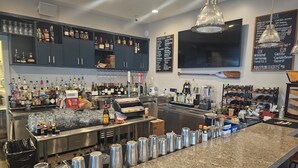 A bar area with a granite countertop, multiple liquor bottles, glasses, and a menu board listing various drinks. - Wildwood Resort & Marina (Granville)