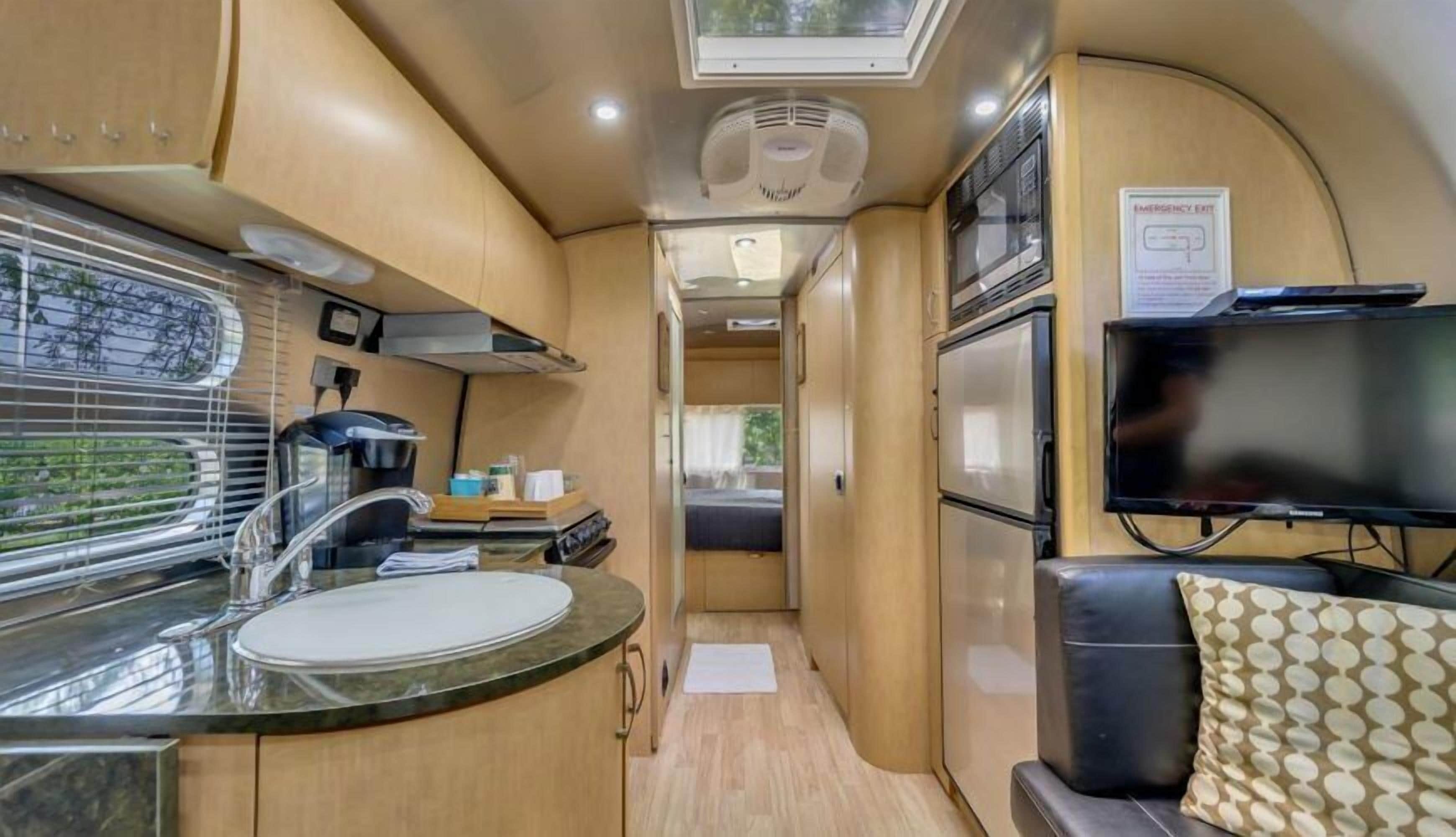 A compact RV interior with a kitchenette, a seating area, a television, and a window.