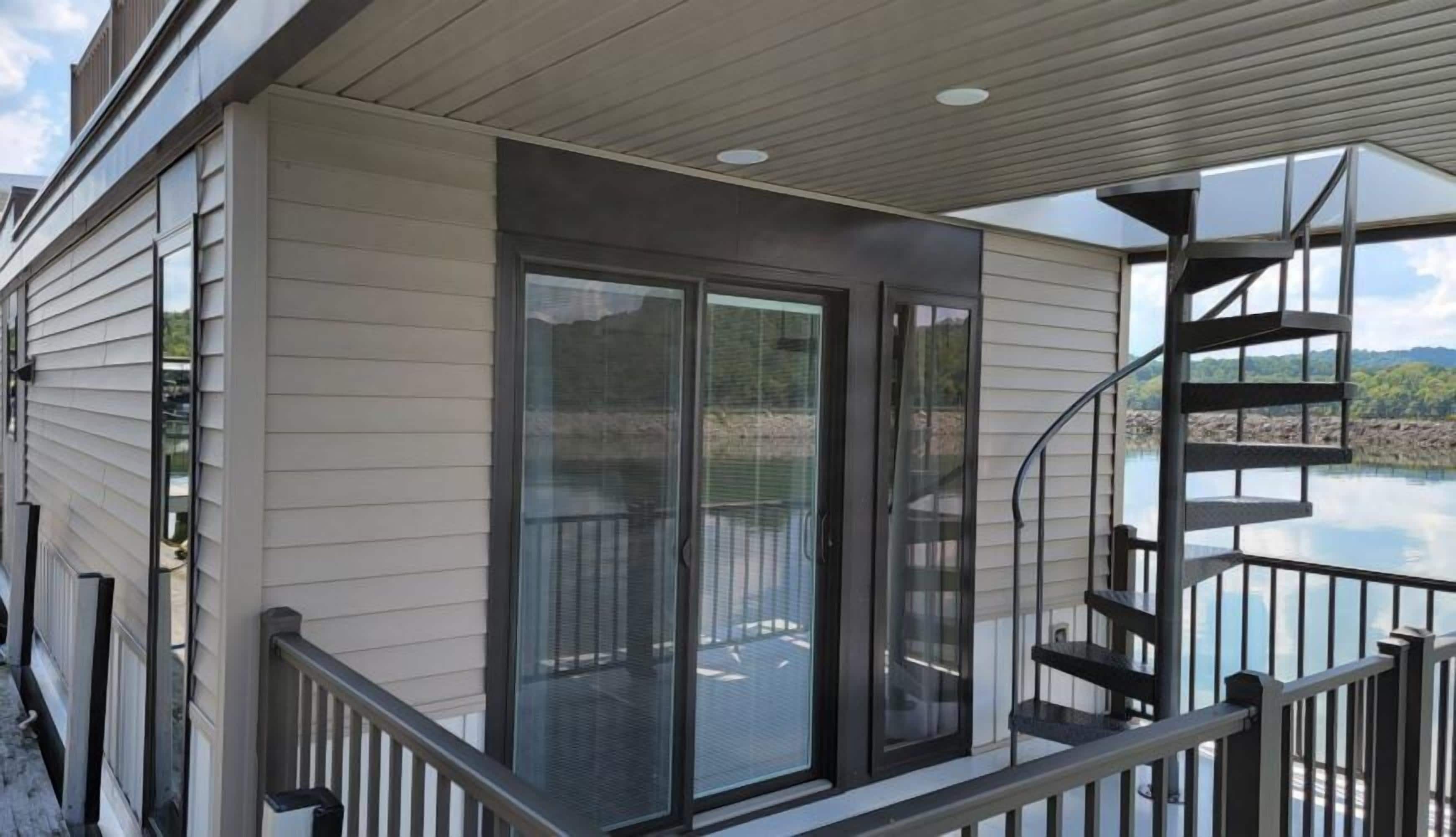 A covered deck with a glass door leading to a pool area, a metal staircase, and a view of a lake.