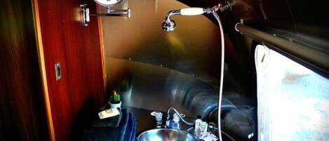 A compact bathroom with a sink, mirror, and shower.