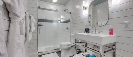 A modern bathroom with a glass-enclosed shower, a white sink with a mirror, and a toilet.