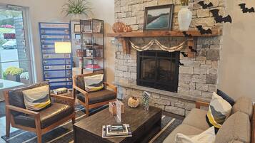 A cozy living room with a stone fireplace, a bookshelf, and comfortable seating.