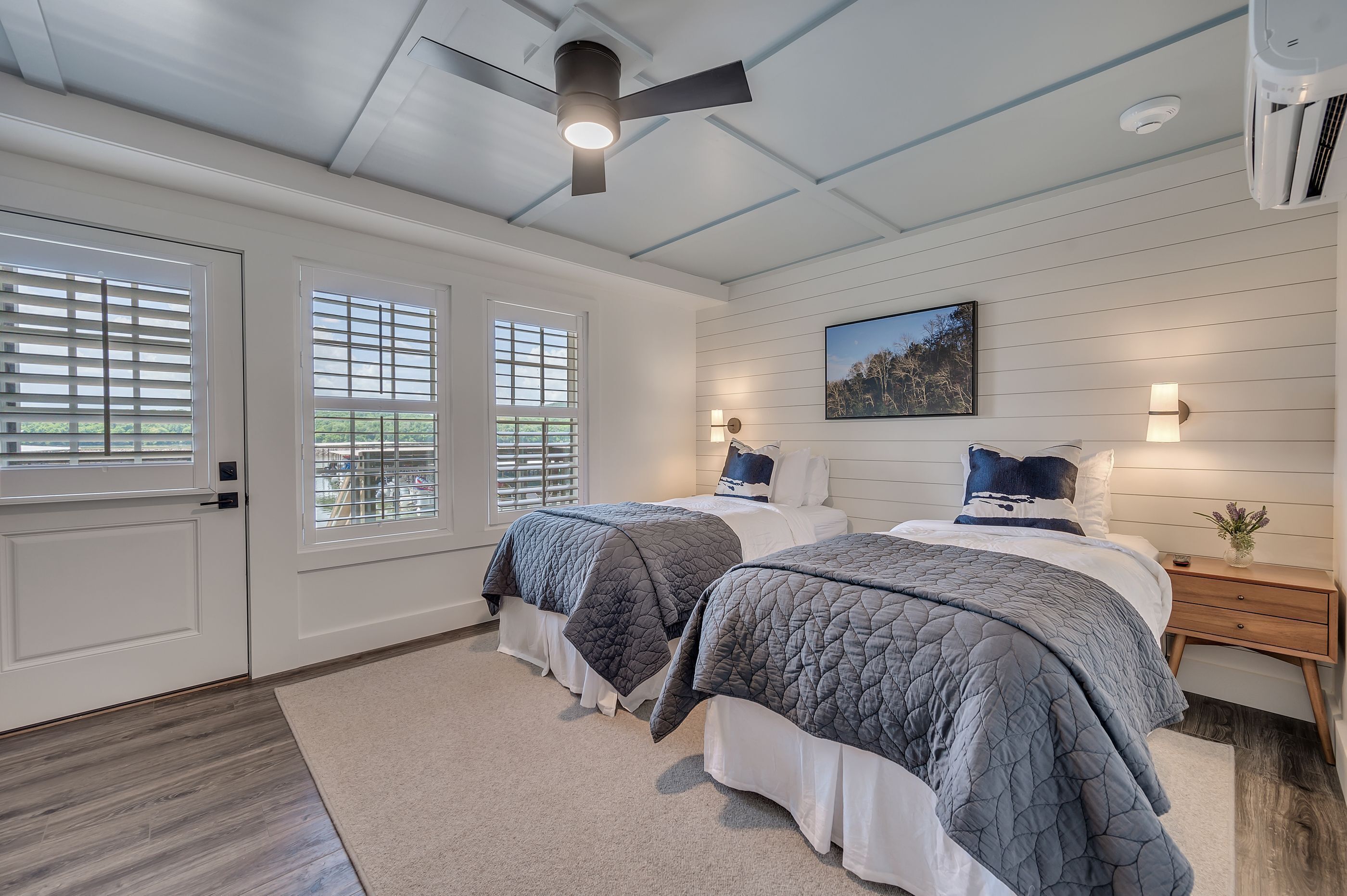 A bedroom with two beds, a ceiling fan, a wall-mounted air conditioner, and a window with blinds.