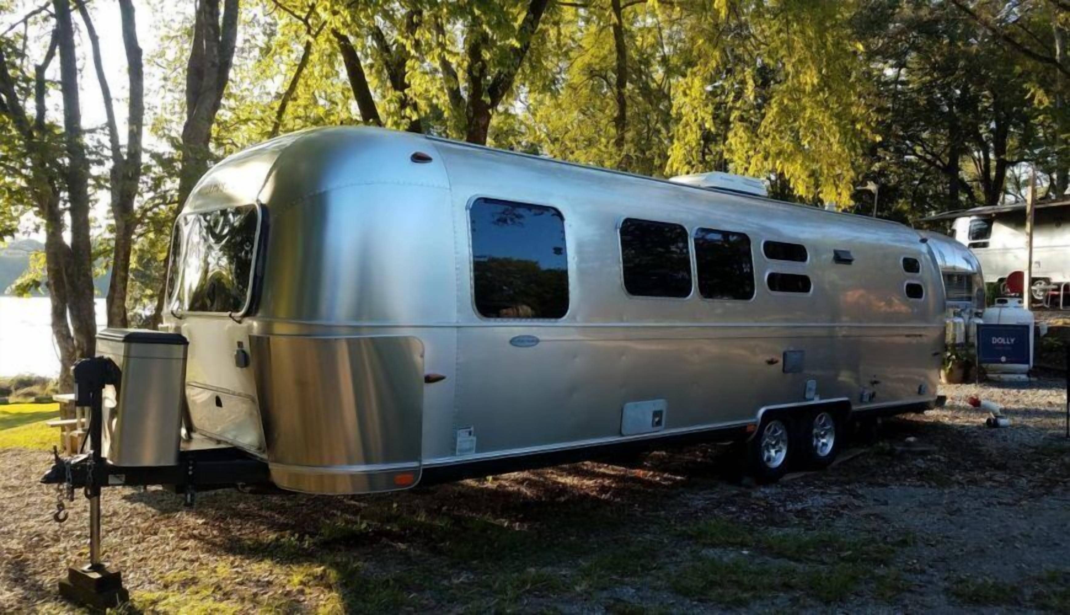 A silver recreational vehicle parked in a wooded area.