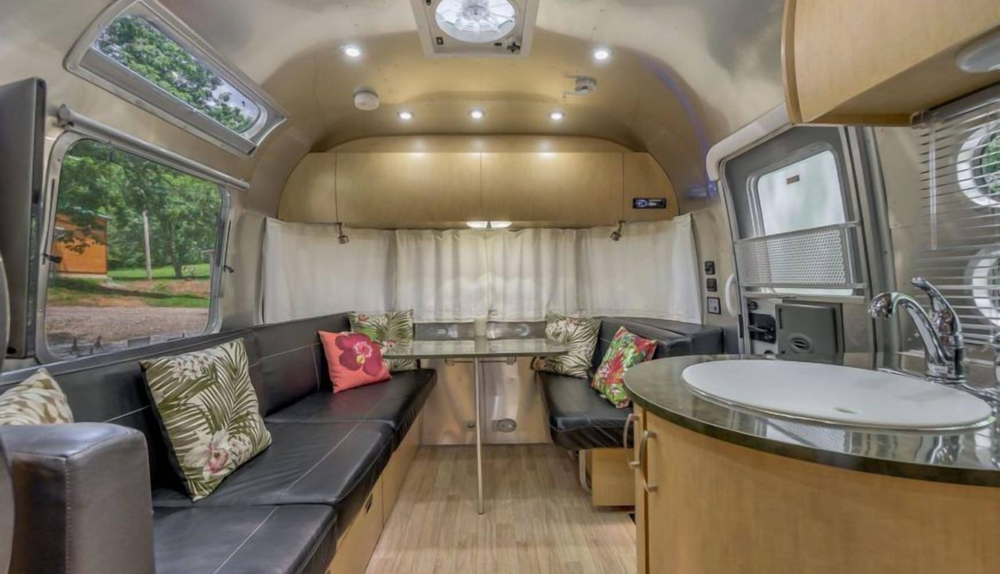 Interior compacto de una caravana con kitchenette, comedor y zona de estar con cojines.