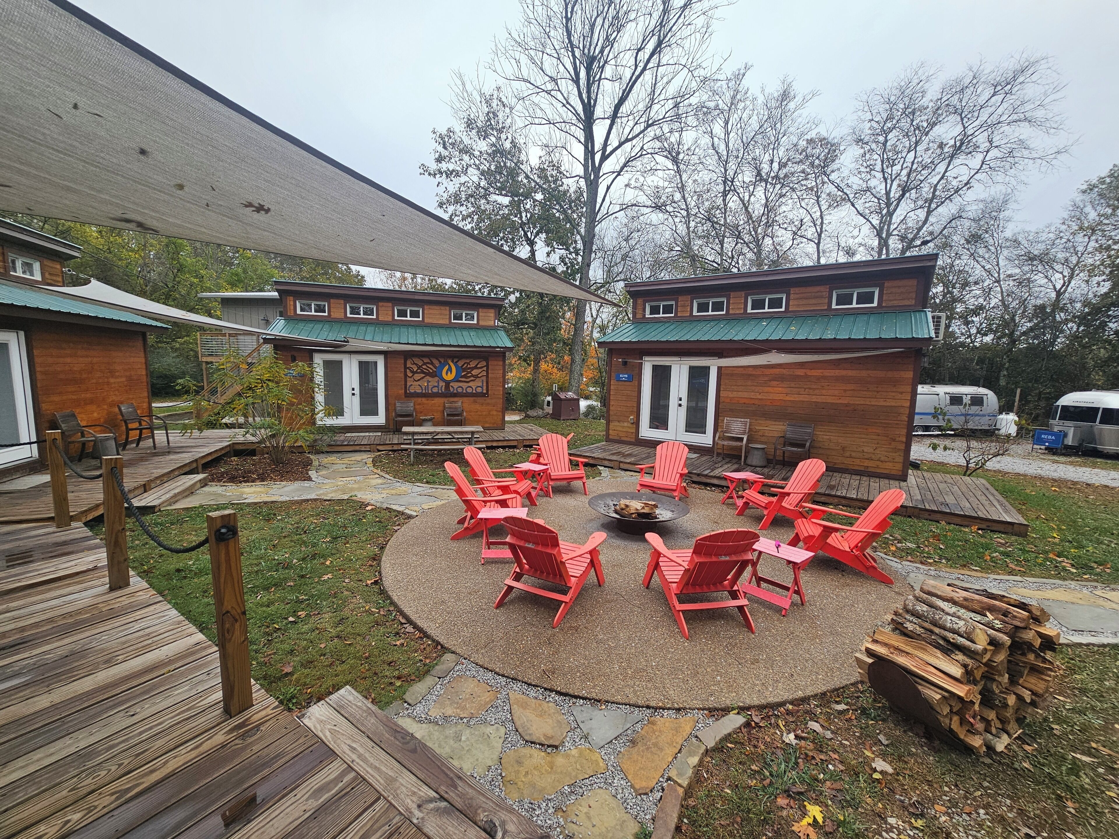 A lodge with a circular patio, red Adirondack chairs, a fire pit, and a stack of firewood.