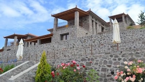 A stone building with multiple balconies, a staircase, and outdoor seating areas with umbrellas. - Villa Molyvos Castle (Lesvos)