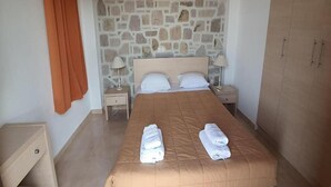 A neatly made bed with two pillows and two folded towels, a stone wall, a wooden wardrobe, and a nightstand with a lamp. - Villa Molyvos Castle (Lesvos)