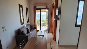 A compact living space with a sofa, a dining table, and a TV mounted on the wall. - Villa Molyvos Castle (Lesvos)