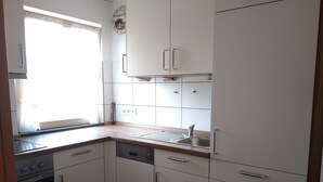 Cocina compacta con armarios blancos, un lavamanos de acero inoxidable y una ventana que proporciona luz natural.