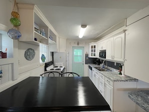 A compact kitchen with white cabinets, a black countertop, and a white door.