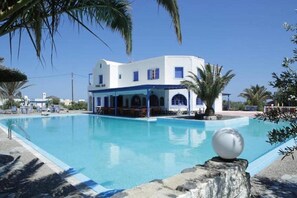 A white building with a pool, palm trees, and a clear blue sky. - Perissa el mar Rooms (Santorini)
