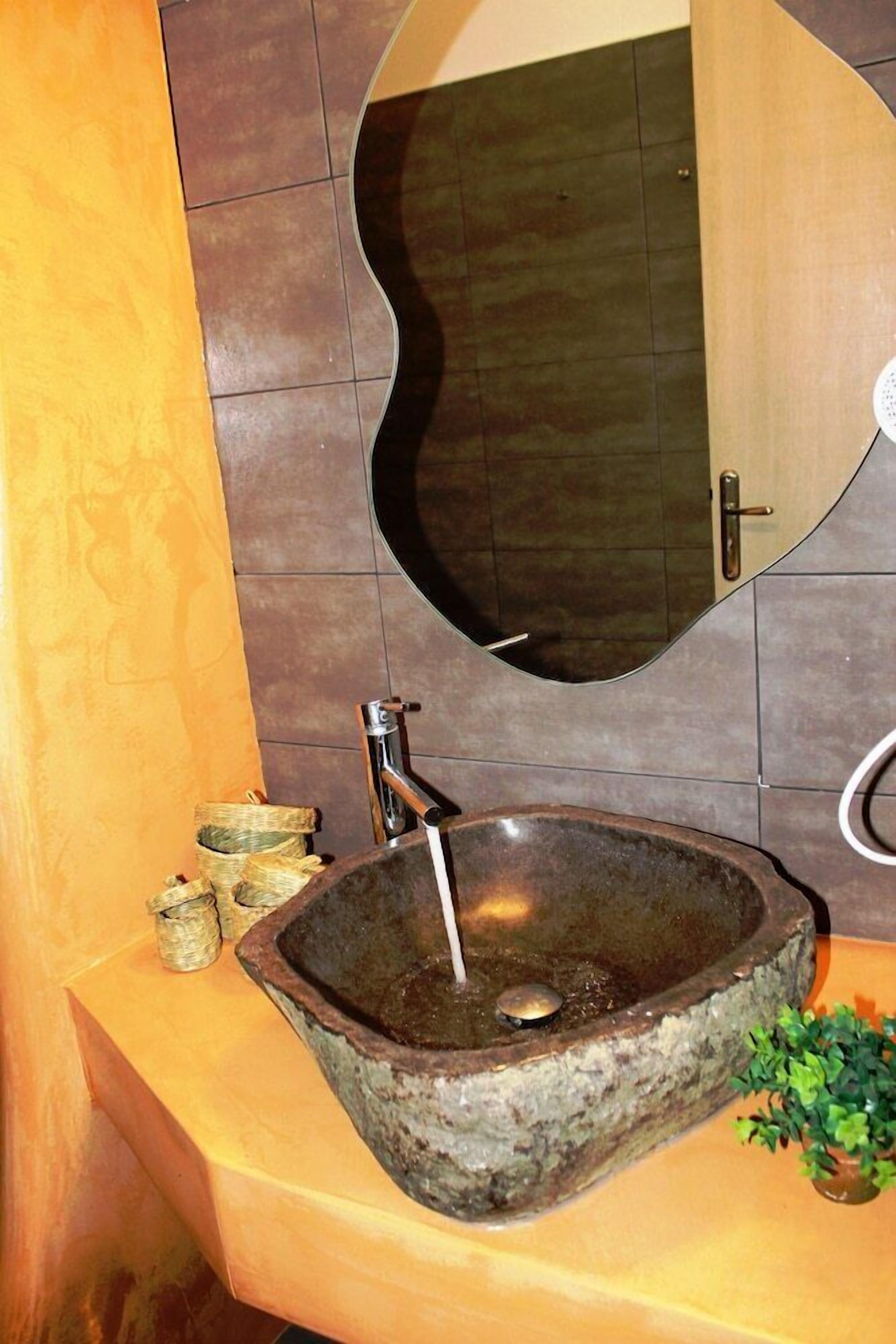 Un lavabo de piedra con un grifo, un espejo encima y una planta pequeña en la encimera.