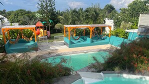 A swimming pool area with two small pools, a slide, and a hammock. - SOUS LES COCOTIERS STUDIO 2 CLIMATISE (Sainte-Rose)