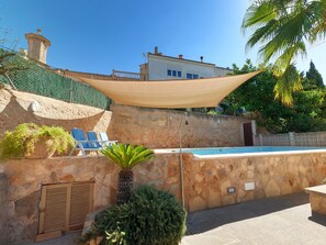 Zona de piscina con muros de piedra, una palmera y un edificio al fondo.