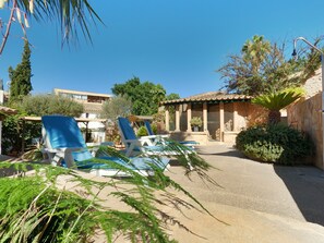 Un área junto a la piscina con sillones de descanso, una pérgola y un edificio de piedra con techo de tejas.
