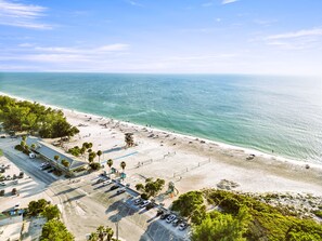 An aerial view of a beach with a parking lot, beach umbrellas, and a lifeguard tower. - Salty Harbor AMI pool retreat near the Beach (Holmes Beach)