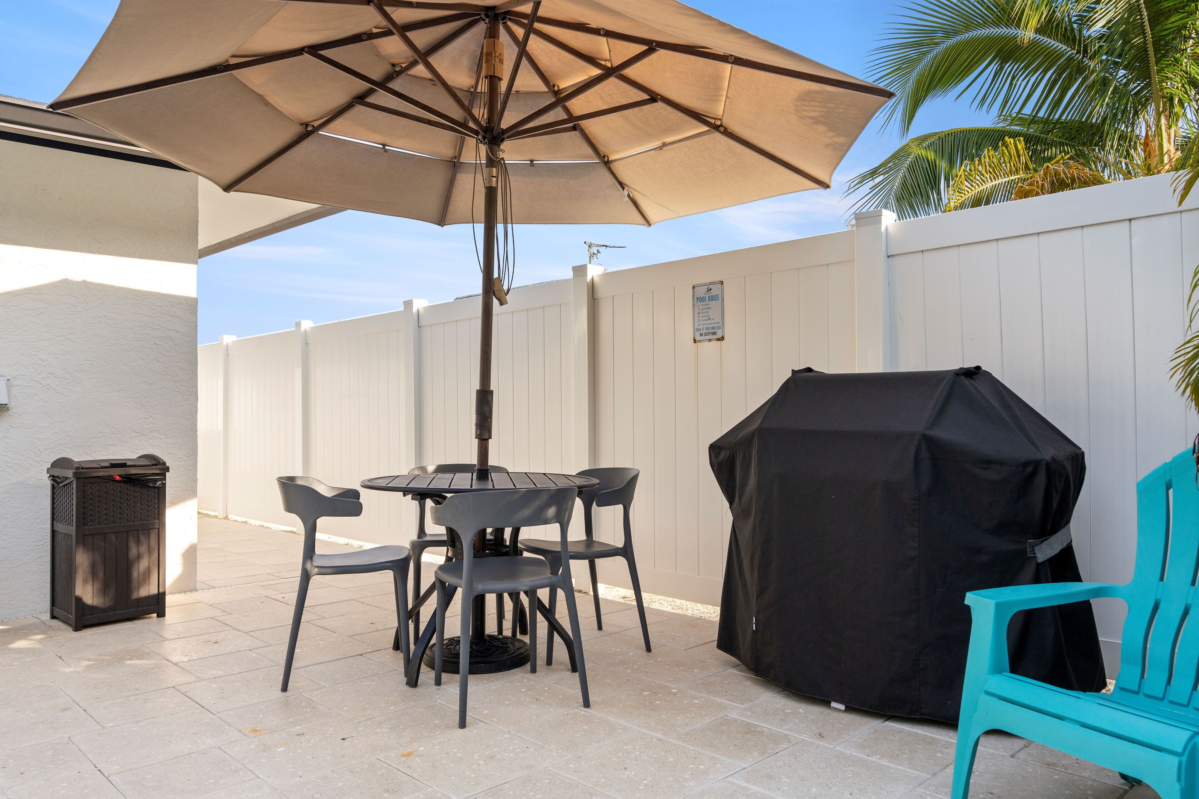 Un espace patio avec une table et des chaises, un barbecue abrité et un parasol.