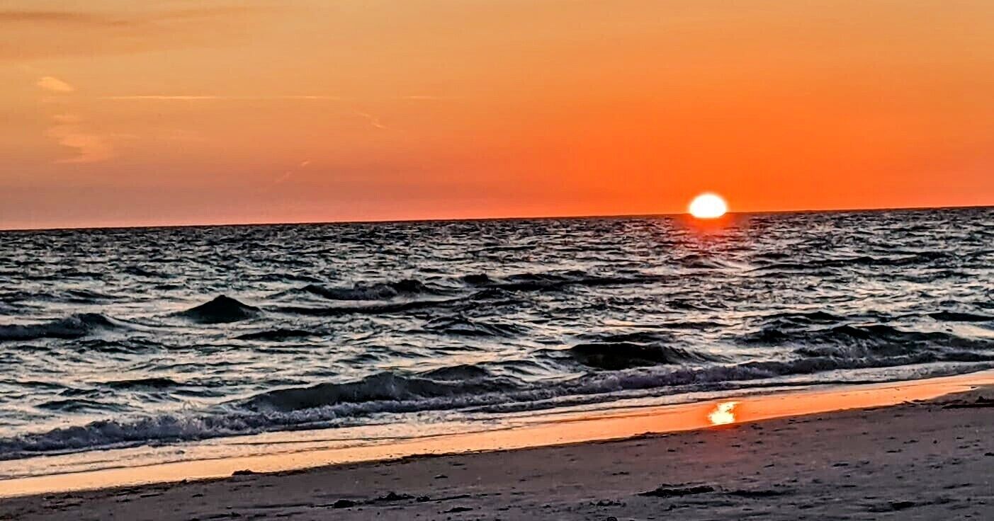 Solnedgang over havet med bølger, der nærmer sig stranden.