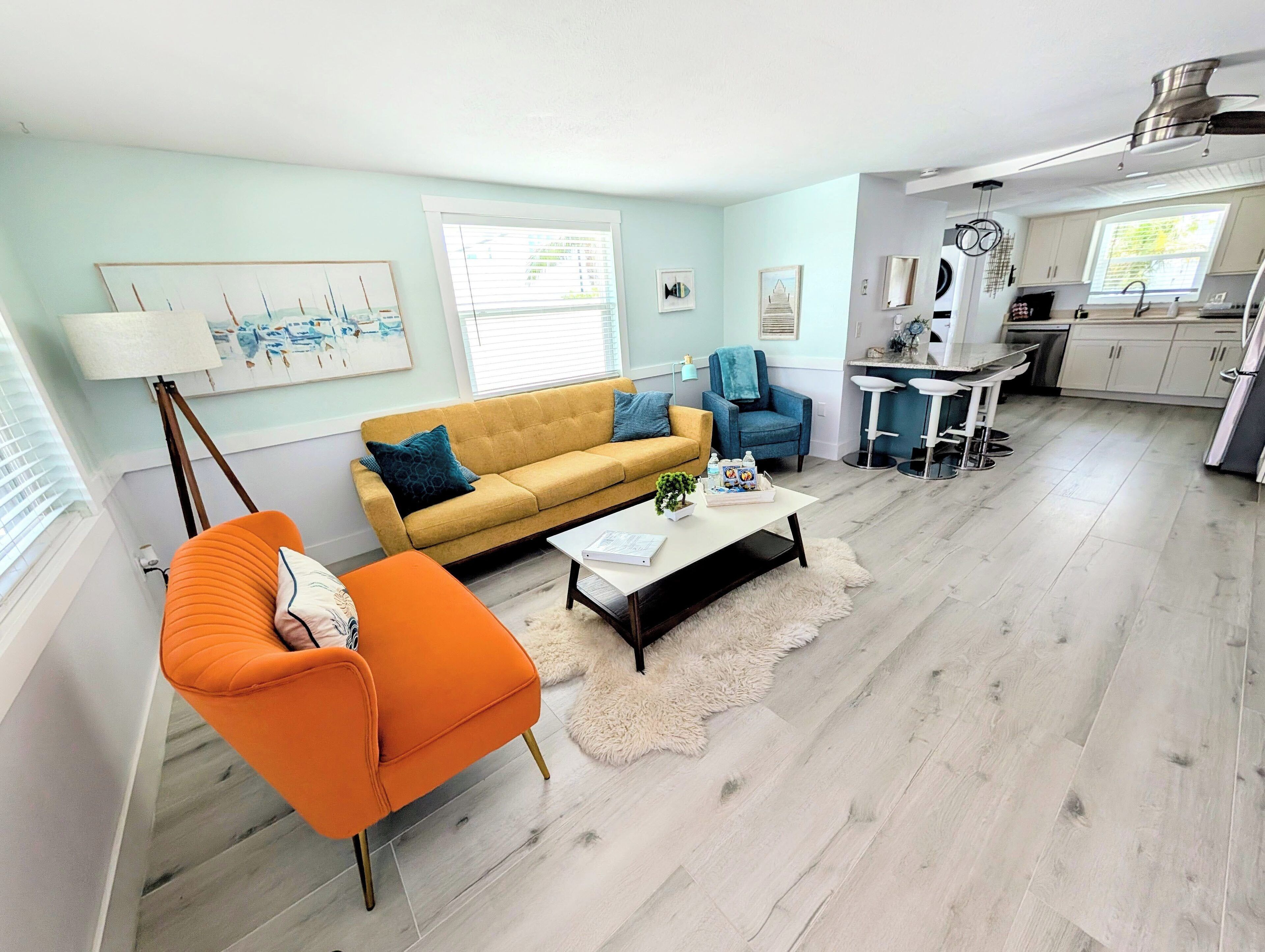 Una sala de estar moderna con sofá, sillón y mesa de centro. Cuenta con una zona de cocina con mesa y sillas.
