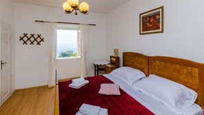 Camera d'albergo con un letto in legno, lenzuola bianche, copripiumino a righe rosse, una finestra con tende, un comodino con una lampada e un quadro appeso al muro.