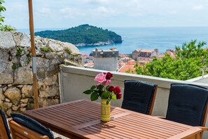 A wooden table with a vase of flowers, a stone wall, and a view of the sea and a distant island. - Two bedroom House Marija with an amazing Old Town view (Dubrovnik)