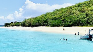 Una spiaggia con acque cristalline turchesi, una riva sabbiosa e una barca ormeggiata a destra.