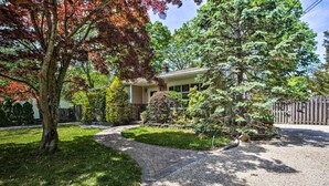 A residential house with a paved driveway, a lawn, and a wooden fence. - Charming Hampton Bays Home 5 Mi to Cooper’s Beach (Hampton Bays)