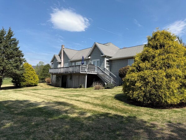 A two-story house with a covered deck, a chimney, and a large yard with mature trees.