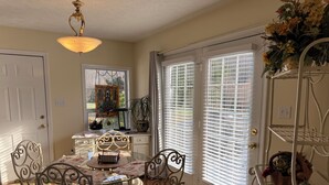 A dining area with a table, chairs, a chandelier, a window with blinds, and a plant.