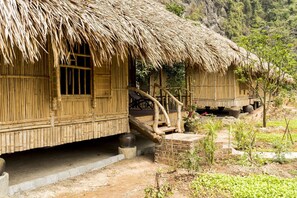 Una casa tradicional de bambú con techo de paja, una escalera de madera y un pequeño jardín.