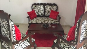 Ein Wohnzimmer mit einem gemusterten Sofa, zwei Sesseln, einem Couchtisch und einem roten Teppich.