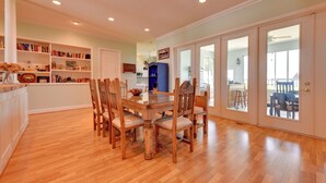 A dining area with a wooden table and chairs, surrounded by bookshelves and a kitchen in the background. - Waterfront Lake Placid Home with Private Dock! (Lake Placid)