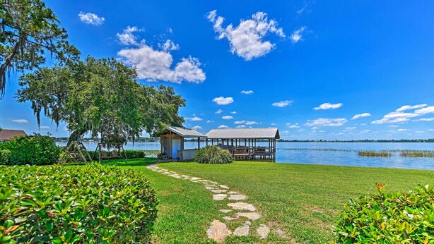 A lakeside property with a wooden dock, a gazebo, and a stone pathway leading to a grassy area. - Waterfront Lake Placid Home with Private Dock! (Lake Placid)