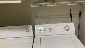 A laundry area with two white front-loading washing machines and a shelf above containing a bag of detergent. - Apartment w/ Pool view 5 min from Galleria (Houston)