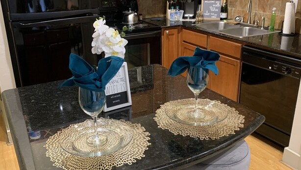 A kitchen with wooden cabinets, a black refrigerator, a microwave, and a coffee maker. There are two stools with blue bows and a sign on the counter. - Apartment w/ Pool view 5 min from Galleria (Houston)