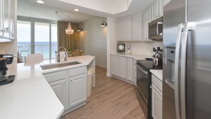 Una cocina moderna con armarios blancos, electrodomésticos de acero inoxidable y vista al océano.