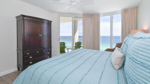 Un dormitorio con una cama grande, un aparador de madera oscura y vista al océano a través de un ventanal corredero.