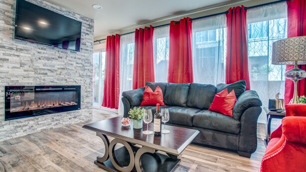 A modern living room with a stone fireplace, a black leather sofa with red cushions, and a wooden coffee table. - Amazing Private Rooftop Deck : Walk to Restaurants! (Dallas)