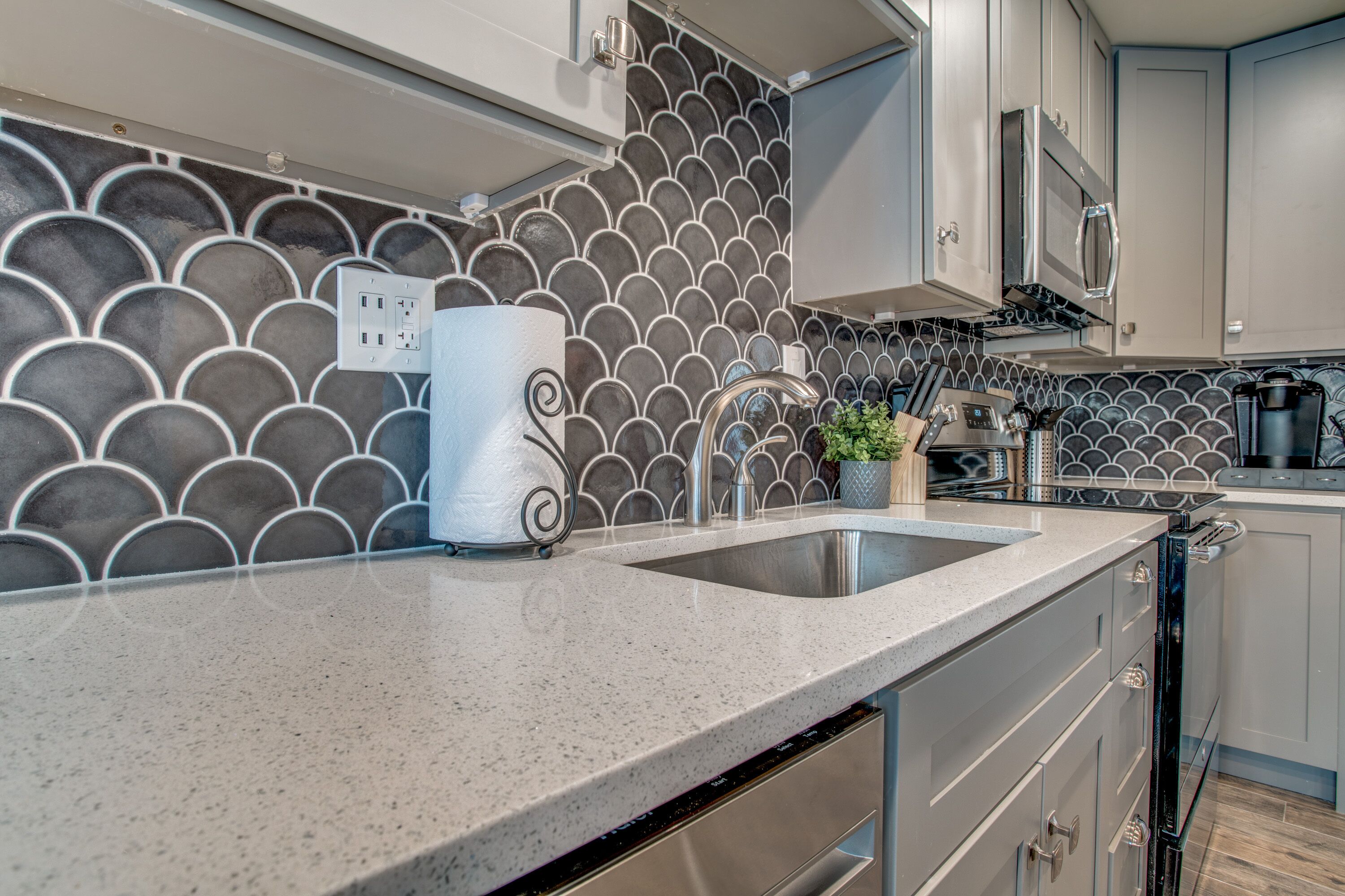 A kitchen with a granite countertop, stainless steel appliances, and a backsplash with a scalloped pattern.