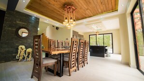 A dining area with a wooden table and chairs, a chandelier, and a stone wall with a circular mirror. - VILLA SEGURA VICENTE (Constanza)