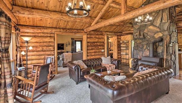 A log cabin interior with a stone fireplace, leather sofas, and a chandelier.
