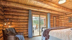 A log cabin bedroom with a bed, a leather chair, and a sliding glass door leading to an outdoor deck.