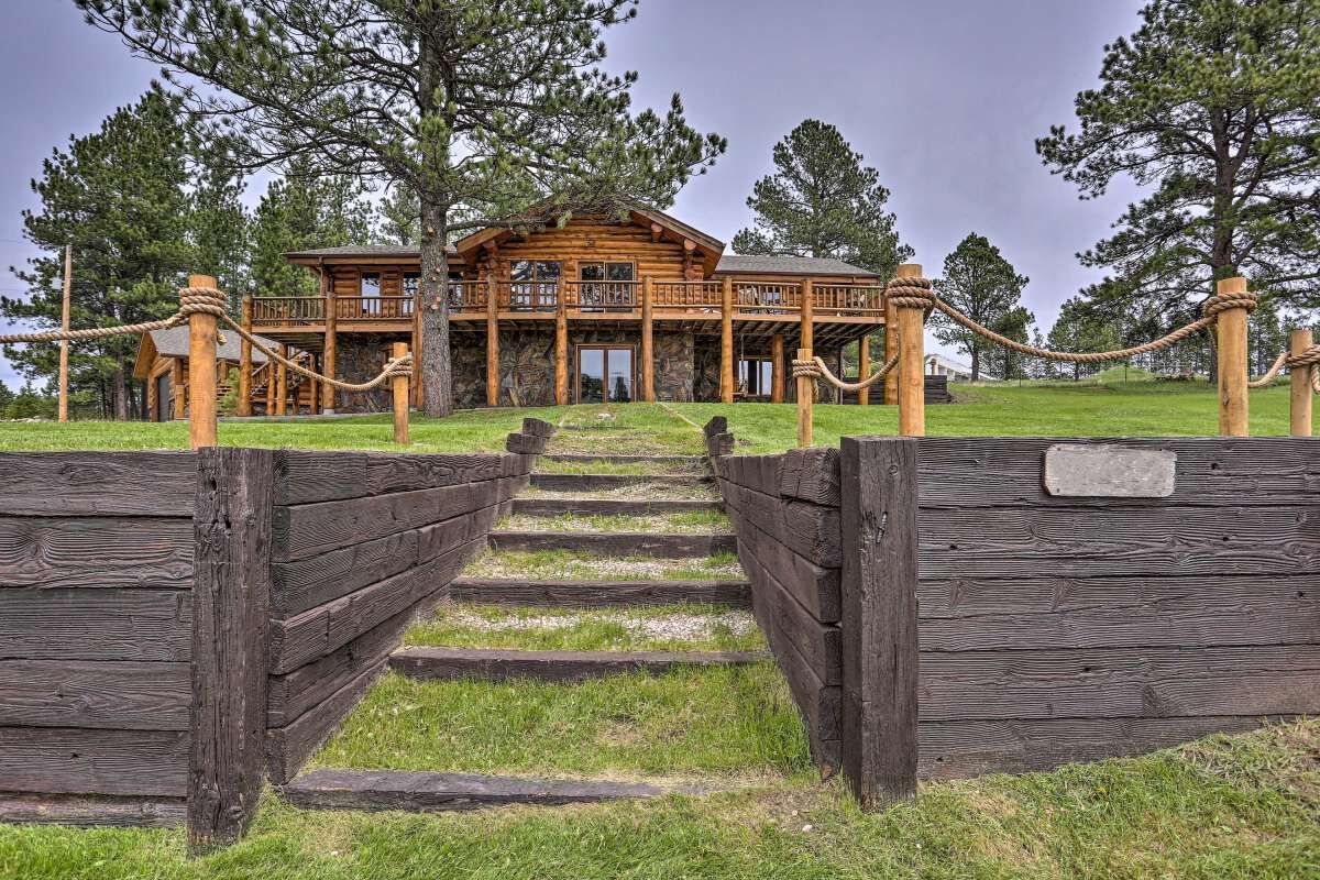 A wooden log cabin with a balcony, surrounded by a wooden fence and a grassy area.