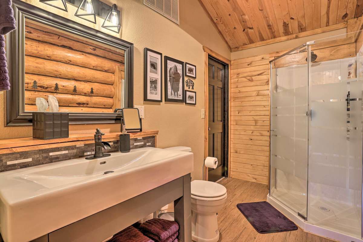Ein Badezimmer mit Holzvertäfelung, Waschbecken, Toilette und einer Duschkabine aus Glas.