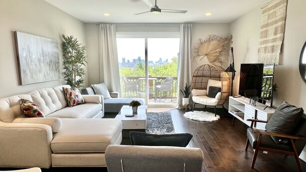 A modern living room with a sofa, armchairs, a coffee table, and a TV. There is a balcony with a view of the city. - Skyline Views/3 Miles to Downtown/WeeklyDiscounts/Pet Friendly (Nashville)