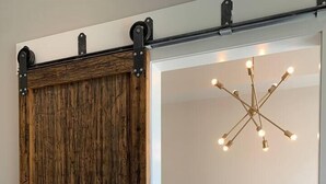 Une pièce dotée d’une porte coulissante en bois de style grange, d’un lustre moderne et d’un coin repas avec des chaises jaunes.